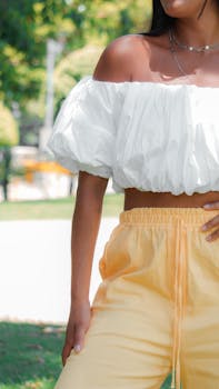 Stylish woman in a white off-shoulder top and orange pants enjoying summer outdoors.