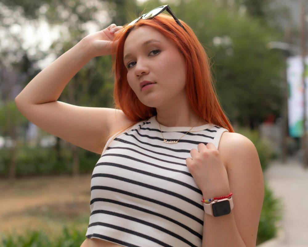 Portrait of a confident red-haired woman wearing sunglasses outdoors in a striped tank top. Stylish and casual look.